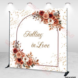 Op de afbeelding: Een witte achtergrond met een bloemenontwerp en de tekst "Falling in Love". Het bloemstuk bevat rode, oranje en witte bloemen. Gouden confetti stippelt de achtergrond. Een donkerbruine boog omlijst de tekst.