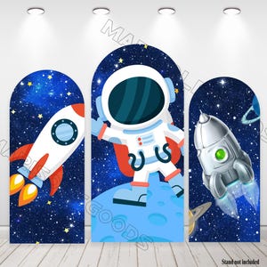 May include: Three blue and black space-themed backdrop panels with an astronaut, rocket, and spaceship. The astronaut is wearing a white spacesuit with a red stripe and is standing on a blue planet. The rocket is white with orange flames and the spaceship is silver with a green window. The panels are arched at the top and have a starry background.
