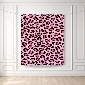 May include: A rectangular fabric backdrop featuring a repeating leopard print pattern. The design consists of irregular black spots and outlines set against a vibrant pink background, creating a bold and high-contrast visual texture across the surface.