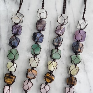 May include: Three brown cord necklaces with seven gemstone beads each. The beads are wrapped in a brown string net and are in the colors of the rainbow. The necklaces have a tassel of smaller gemstones at the bottom.