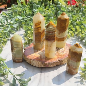 May include: Five polished green and brown onyx crystal points on a wooden slice. The points are all different sizes and shapes, and they have a natural, earthy look.