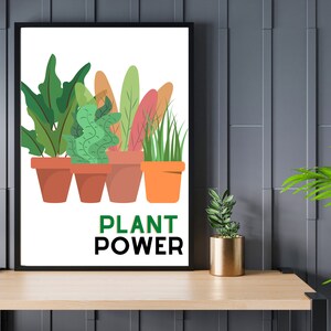 Può includere: Una stampa incorniciata con sfondo bianco che presenta cinque piante in vaso con foglie verdi e accenti colorati. Il testo "PLANT POWER" è stampato in nero sotto le piante.