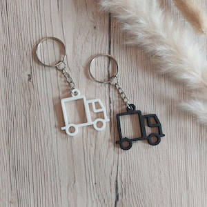 May include: Two keychains featuring a truck silhouette, one in white and one in black. Each keychain consists of a flat, outlined truck shape attached to a metal split ring by a short silver-toned chain link, creating a simple, functional design.