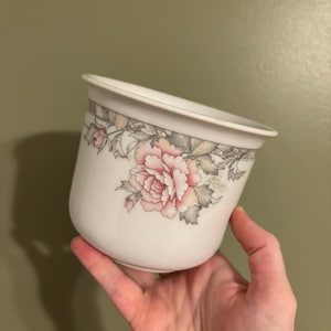 May include: White ceramic planter with a floral design featuring pink and gray roses and leaves.