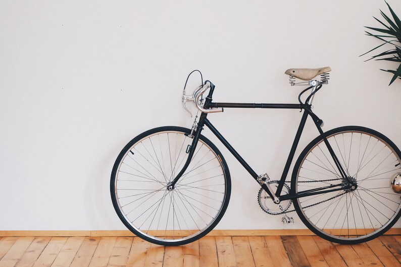 May include: A black bicycle with a brown leather saddle, thin tires, and a white wall background.