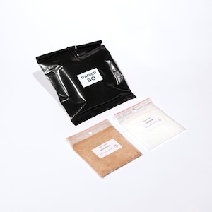 May include: Two small clear plastic bags containing white powder and brown powder. The bags are labelled "Fixateur" and "Développer". A black plastic bag with the text "Papier 50" is also in the image.