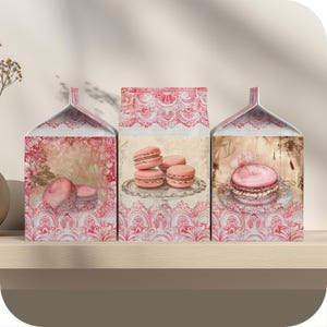 May include: Three pink and white cardboard boxes with a vintage floral design and pink macarons on the front. The boxes have a lace trim and are perfect for storing small items.