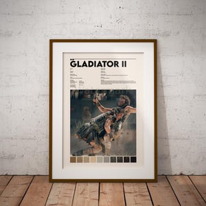 Könnte beinhalten: Ein Filmplakat für den Film "Gladiator II" mit einer Szene von zwei Männern, die in einer staubigen Arena kämpfen. Das Plakat ist in einem braunen Rahmen und hat eine Farbpalette aus Braun-, Beige- und Grautönen.