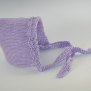 May include: A lavender knitted baby bonnet with a decorative edge and long ties.