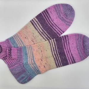 Könnte beinhalten: Ein Paar gestreifte Socken in den Farben Rosa, Lila, Blau und Beige. Die Socken sind gestrickt und haben einen gerippten Bund.