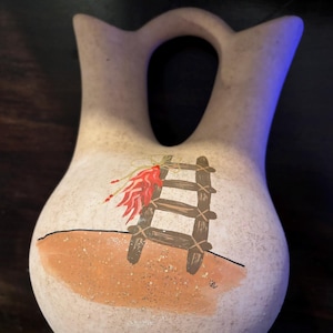 May include: A white ceramic pitcher with a brown ladder and red chili peppers painted on it. The pitcher has a unique shape with a handle that forms a loop at the top.