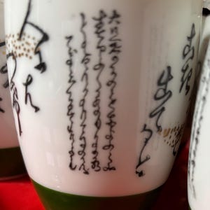 Sake/tea cups set of 5, white with black lettering, green base, marked on bottom.