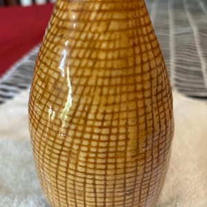 May include: A small, brown ceramic vase with a grid pattern. The vase has a rounded body and a narrow neck. The grid pattern is made up of thin, dark brown lines. The top of the vase is a lighter shade of brown.