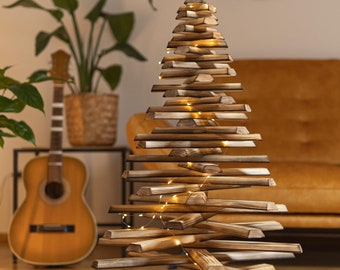 May include: A wooden Christmas tree made of stacked wood planks with a rustic finish. The tree is decorated with warm white fairy lights.