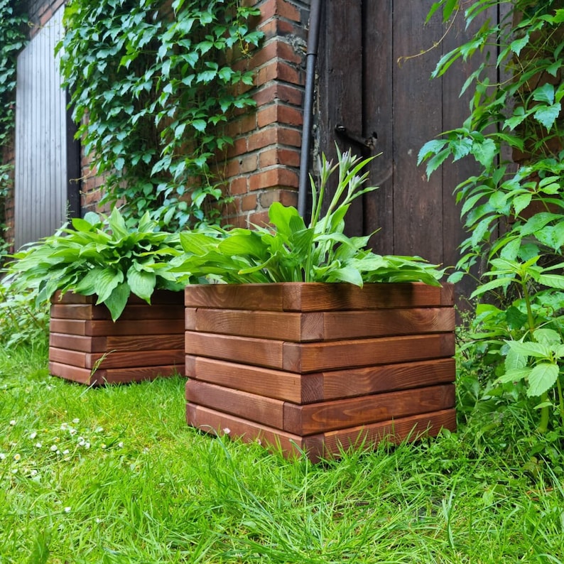 May include: Two wooden planter boxes with brown stain, one on top of the other, filled with green plants. The boxes are made of horizontal planks.