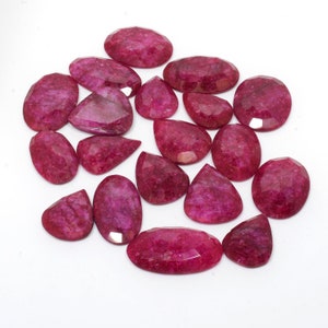 May include: A collection of 17 faceted ruby gemstones in various shapes and sizes. The stones are a deep red color with a slight sparkle.