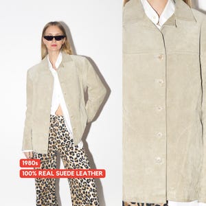Pu&ograve; includere: Giacca in camoscio beige chiaro con chiusura a bottoni, colletto e maniche lunghe. La giacca &egrave; abbinata a una camicia bianca e pantaloni con stampa leopardata. I testi "1980s" e "100% REAL SUEDE LEATHER" sono visibili.