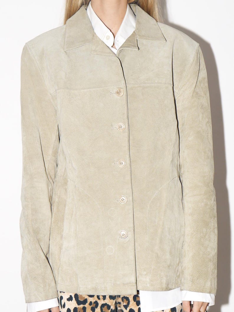 Pu&ograve; includere: Giacca in pelle scamosciata beige chiaro con collo e chiusura con bottoni. La giacca ha un design classico con una vestibilit&agrave; sartoriale, chiusura con bottoni e una finitura sottile e strutturata. La giacca &egrave; di colore neutro, adatta a vari outfit.