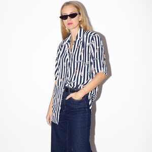 May include: A short-sleeved, button-down shirt with vertical navy blue and white stripes. The shirt features a pattern of small, colorful designs. Paired with dark wash, wide-leg jeans and a black belt.