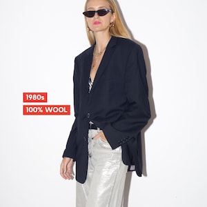 May include: A black wool blazer from the 1980s. The blazer is paired with silver pants and sunglasses. The text "1980s" and "100% WOOL" are in a red rectangle.