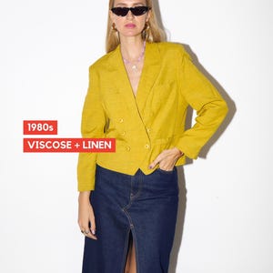 May include: A yellow double-breasted blazer made of viscose and linen, paired with a dark denim skirt. The blazer has a textured appearance and is from the 1980s. The skirt has a front slit. The text "1980s" and "VISCOSE + LINEN" are visible.
