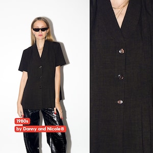 May include: Black short-sleeved top with a V-neck and three buttons. The top is part of a vintage collection from the 1980s, as indicated by the text in the image. The brand is Danny and Nicole.