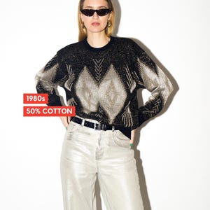 Puede incluir: Un suéter vintage negro y dorado con un patrón geométrico. Se combina con vaqueros grises claros y un cinturón negro. El texto "1980s" y "50% COTTON" es visible en un recuadro rojo.
