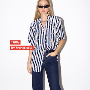 May include: A vintage button-down shirt with vertical navy and white stripes, featuring a colorful pattern. The shirt is paired with dark wash denim jeans. The text "1980s by Francoise&reg;" is visible in the image.