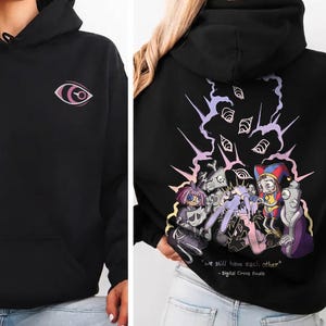 May include: A black hooded sweatshirt featuring a small pink eye graphic on the front chest. The back displays a colorful illustration of animated characters with multiple eyes above them and the text "we still have each other" and "Digital Circus Finale".