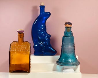 3 botellas de vidrio de colores con formas únicas.