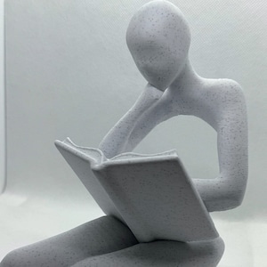 Könnte beinhalten: Eine weiße, abstrakte Skulptur einer Person, die sitzt und ein Buch liest. Die Skulptur ist aus einem strukturierten Material gefertigt, das an Beton erinnert.