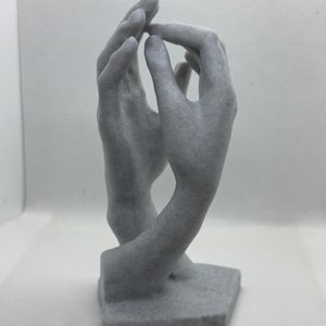 May include: A gray, sculpted, abstract sculpture of two hands clasped together. The sculpture is on a gray base.