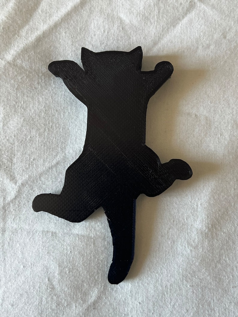 Op de afbeelding: Een zwart 3D-geprint kattenbeeldje in een speelse pose met uitgestrekte poten en een opgerolde staart.