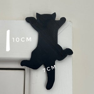 Op de afbeelding: Zwarte kat silhouet wanddecoratie, 10 cm hoog en 7 cm breed. De kat is in een klimhouding met uitgestrekte poten.