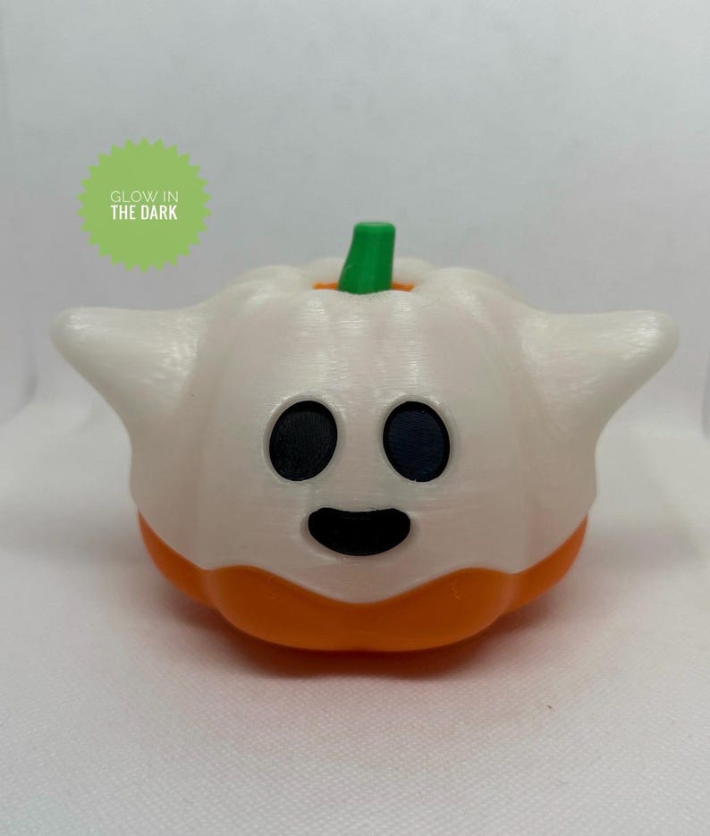 May include: A white and orange Halloween decoration in the shape of a ghost-pumpkin hybrid. The ghost-pumpkin has black eyes and a smiling mouth. The stem is green. The text "GLOW IN THE DARK" is in a green circle.