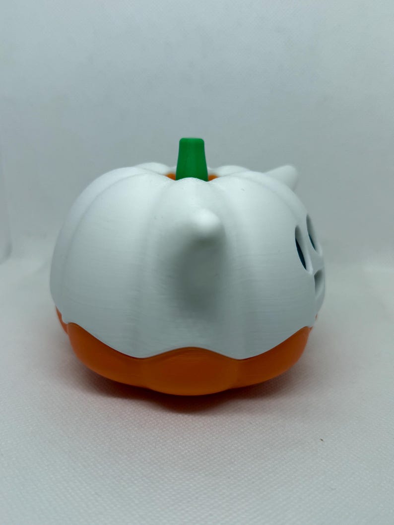 May include: A white and orange Halloween pumpkin decoration with a green stem. The pumpkin has a ghost-like design with cut-out eyes and a small horn. The base of the pumpkin is orange.