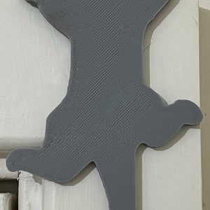 Op de afbeelding: Een grijze 3D-geprinte katten-silhouet deurstop. De kat staat in een springende pose met zijn poten omhoog.