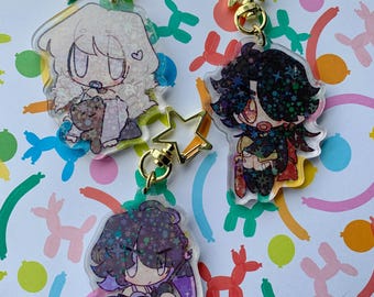 Op de afbeelding: Drie acryl sleutelhangers met cartoon karakter ontwerpen. Elke sleutelhanger heeft een ander karakter met gouden stervormige sluitingen. De karakters hebben verschillende haarkleuren en outfits, met één die een teddybeer vasthoudt.