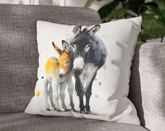 May include: A decorative throw pillow featuring a watercolor painting of two donkeys. The adult donkey is dark gray and black, while the foal is orange and white. The pillow has a white background with colorful paint splatters.