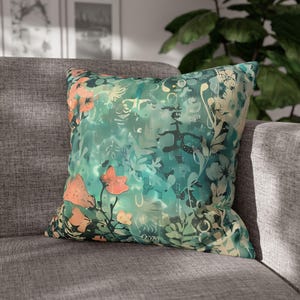 May include: Square decorative pillow with a teal and green abstract floral design. The pillow features coral-colored flowers and a mix of botanical and artistic elements. The pillow is placed on a gray sofa.