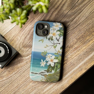 Pu&ograve; includere: Una custodia per telefono con un design floreale con fiori bianchi e foglie verdi su uno sfondo di oceano blu.