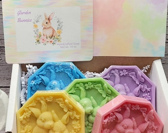 May include: A white gift box with a lid that says "Garden Bunnies" and "Handmade Soap, Net Wt. 1 oz."  The box contains five octagonal soaps with bunny designs in shades of blue, green, yellow, pink, and purple.