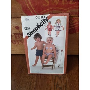 May include: Vintage Simplicity sewing pattern for a size 3 toddler. The pattern features illustrations of children's clothing, including swimwear and outfits. The package is in a cardboard sleeve with the Simplicity logo and product number 6010.