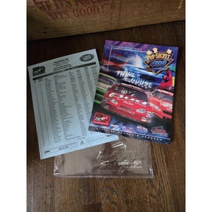 Può includere: Una collezione di cimeli di corse, tra cui un programma souvenir della gara Pop Secret 400, un foglio di partenza e un souvenir del North Carolina Speedway. Il programma presenta un'auto da corsa rossa.