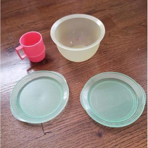 Könnte beinhalten: Ein Set aus vier Plastiktellern in Grün und Weiß. Zwei der Teller sind rund und haben einen erhöhten Rand. Die anderen beiden Teller sind kleiner und haben einen Griff. Es gibt auch eine rosa Plastiktasse mit einem Griff.