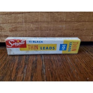 以下が含まれることがあります： ヴィンテージのScripto鉛筆芯の箱。箱は白で、赤、黄、青の文字が書かれています。テキストは「Scripto」、「12 Black Thin Leads」、および「20¢」と書かれています。箱は長方形で、段ボールでできているようです。