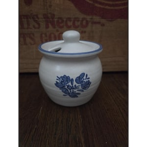 Könnte beinhalten: Ein kleines, weißes Keramikgefäß mit Deckel. Das Gefäß hat ein blaues Blumenmuster und einen blauen Rand. Der Deckel hat einen kleinen Knopf und ein Loch. Das Gefäß steht auf einer Holzoberfläche.