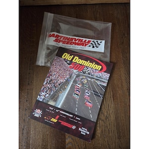 Peut inclure: Un sac en plastique transparent contenant un autocollant Martinsville Speedway blanc et rouge et un programme de course. La couverture du programme présente le texte "Old Dominion 500" et une scène de circuit. Le programme commémore le 55e anniversaire de la course.