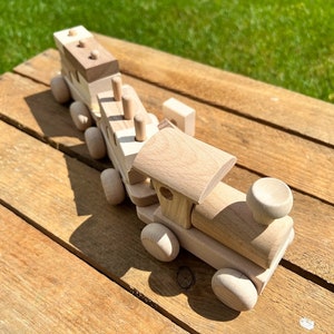 Könnte beinhalten: Ein hölzerner Spielzeugzug mit mehreren Wagen, darunter eine Lokomotive mit abgerundetem Dach und einem Schornstein. Der Zug ist aus Naturholz gefertigt und hat eine hellbraune Farbe.