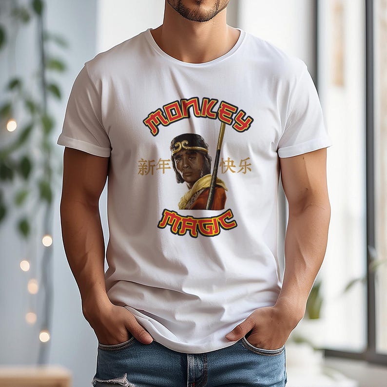 May include: White t-shirt featuring a graphic of a person with a staff, the text "MONKEY MAGIC", and Chinese characters. The design is in red and yellow. The shirt is a crew neck.